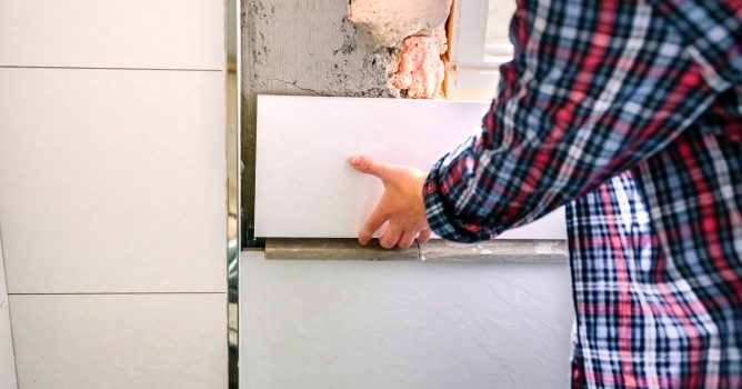 Unrecognizable female bricklayer laying tile on the wall Detail of hand of unrecognizable female bricklayer laying tile on the wall in bathroom renovation